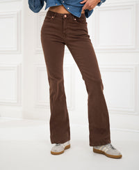Person wearing brown flared PLEIN PUBLIQUE jeans in a white paneled room.