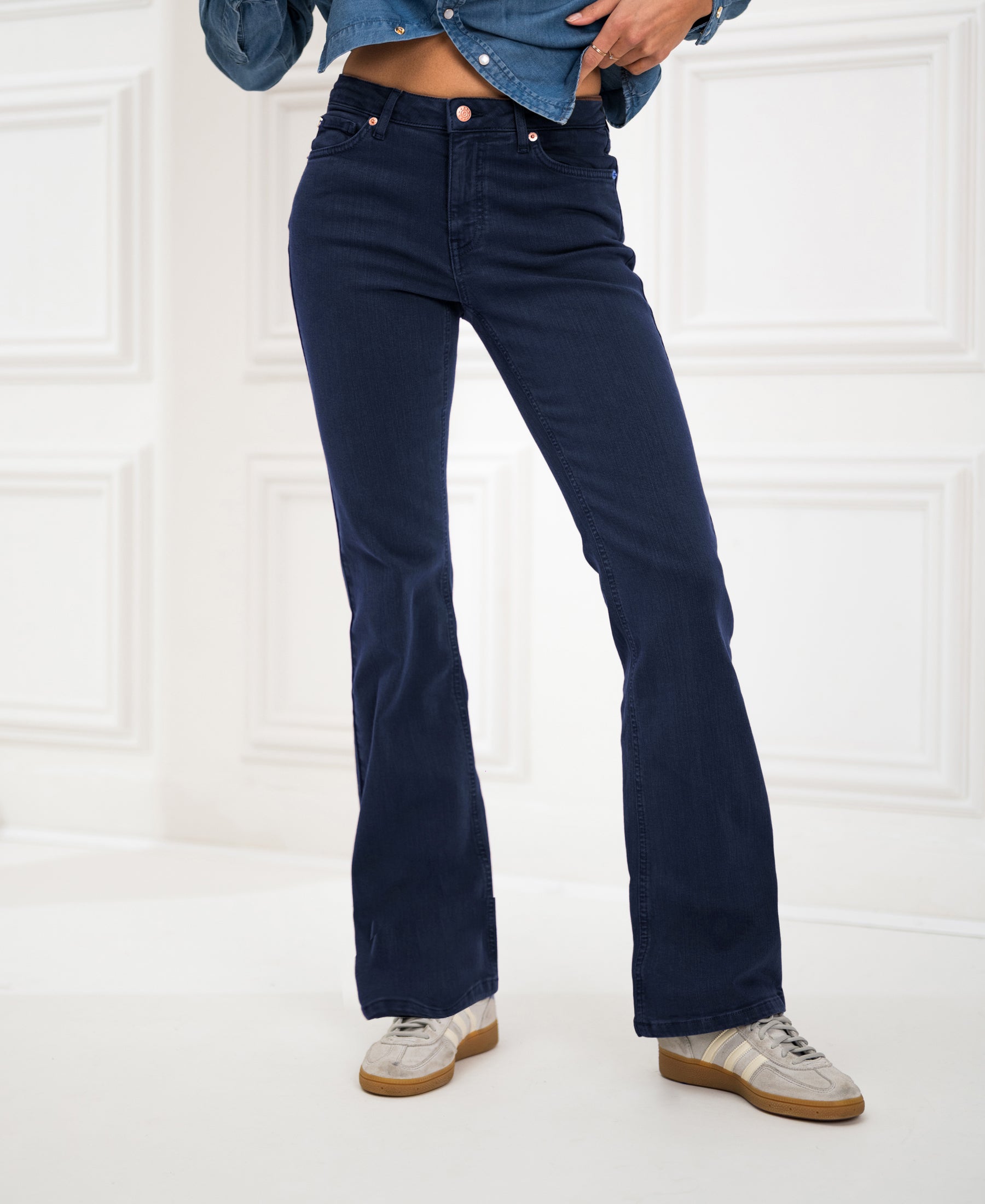 Person wearing dark blue flared jeans in a bright paneled room.