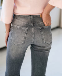 Person wearing grey stonewash flared jeans, hand in back pocket.