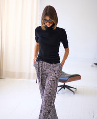 Black LE FRANCOIS short-sleeve turtleneck sweater shown indoors, model with hands in pockets.