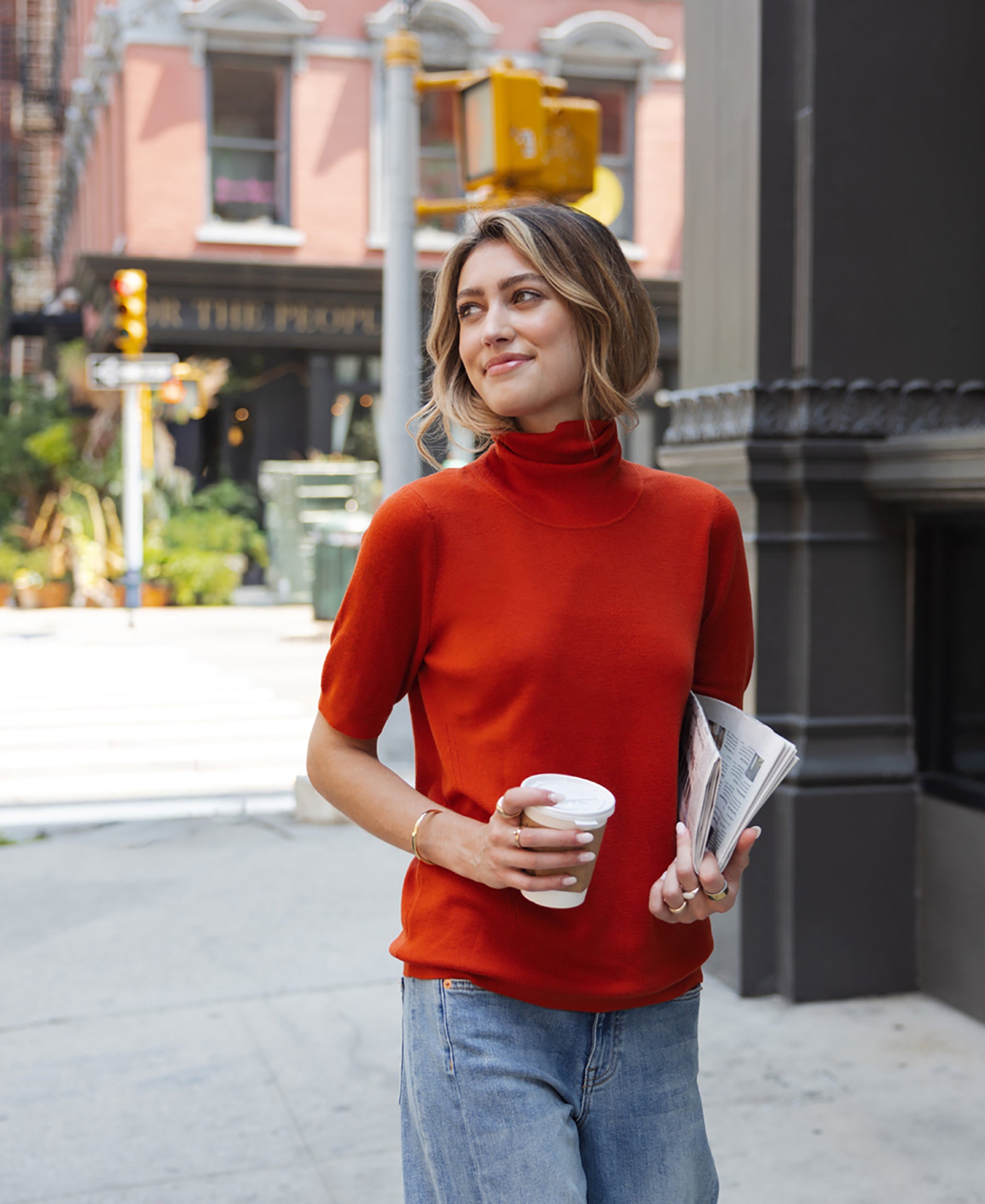 Woman wearing a cayenne short sleeve turtleneck smiles on the sidewalk.