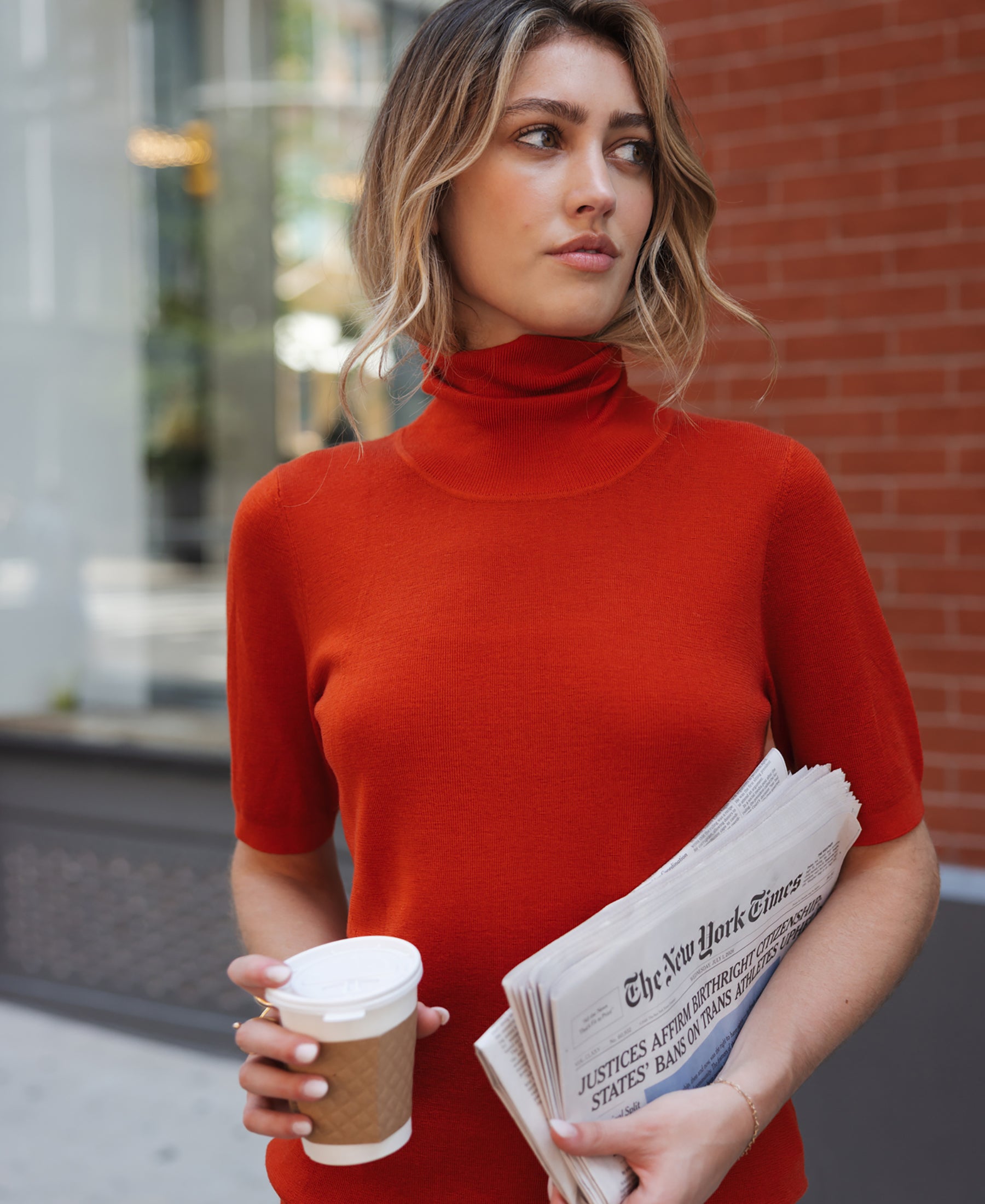 Woman wearing a red short-sleeve turtleneck sweater in an urban setting.