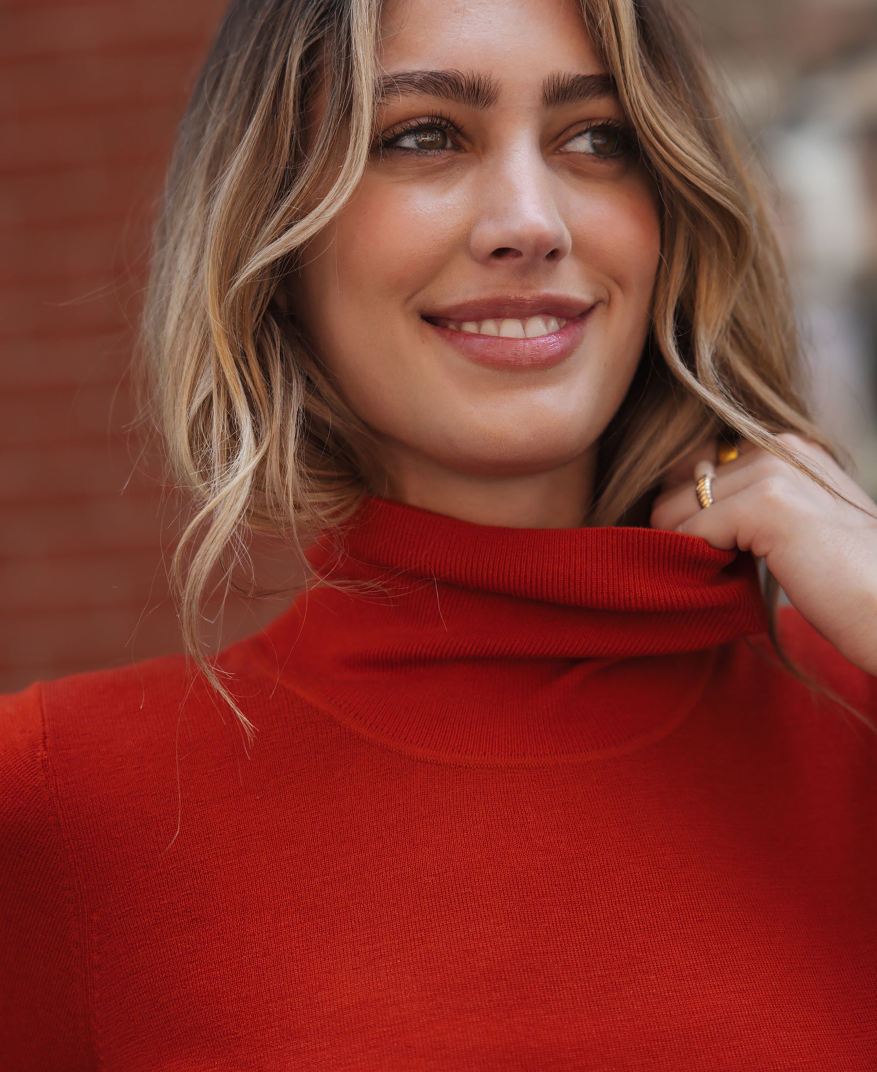 Woman wearing a red short-sleeve turtleneck sweater, standing by a brick wall outdoors.