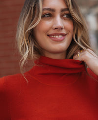 Woman wearing a red short-sleeve turtleneck sweater, standing by a brick wall outdoors.
