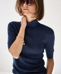 Woman wearing a short sleeve turtleneck sweater in blue, on a white background.
