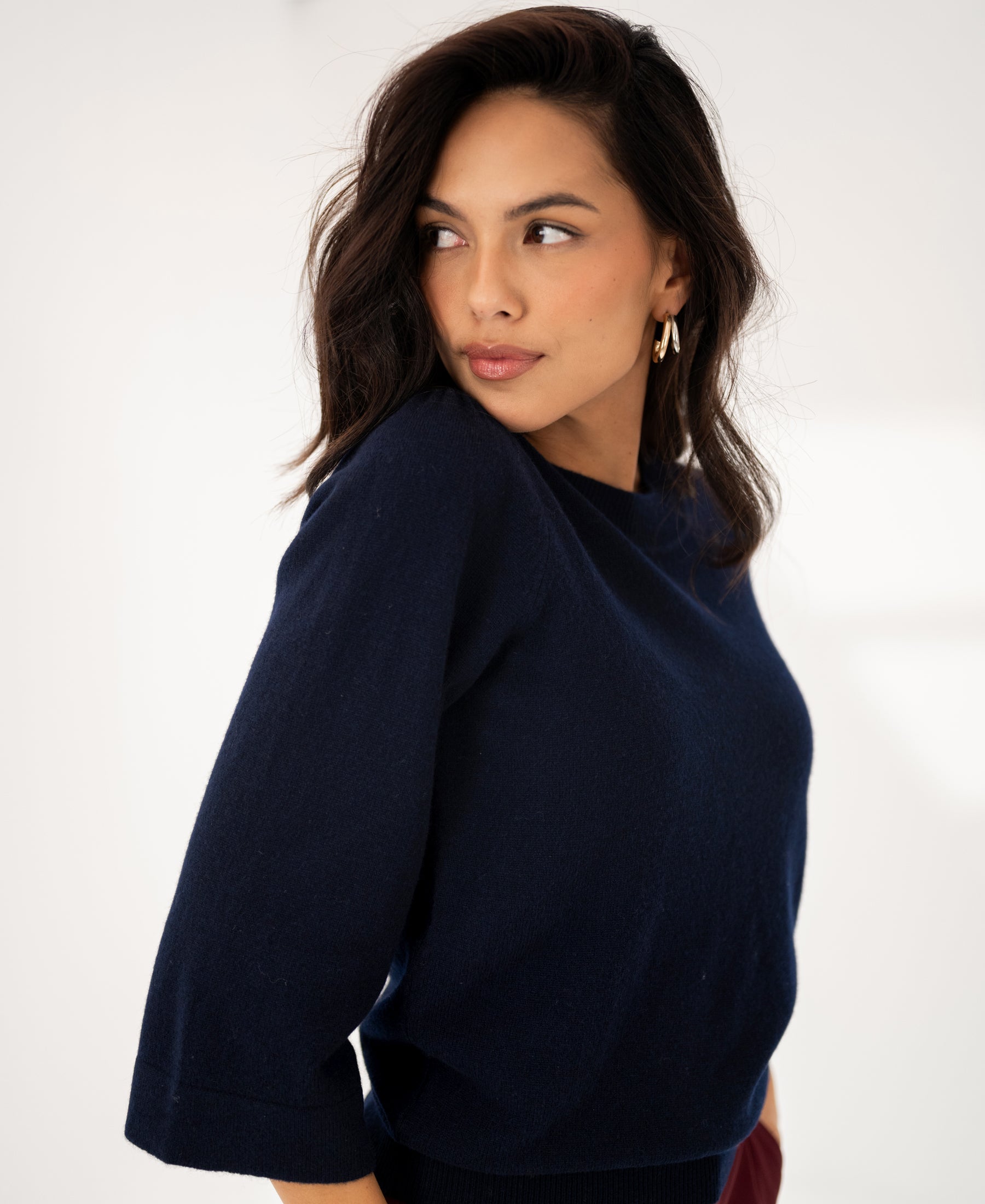 Navy blue merino wool sweater, worn by a woman with wavy dark hair, shown from the side against a neutral background.