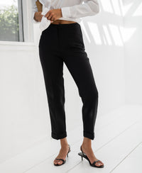 Black cropped trousers in a bright room with white walls.