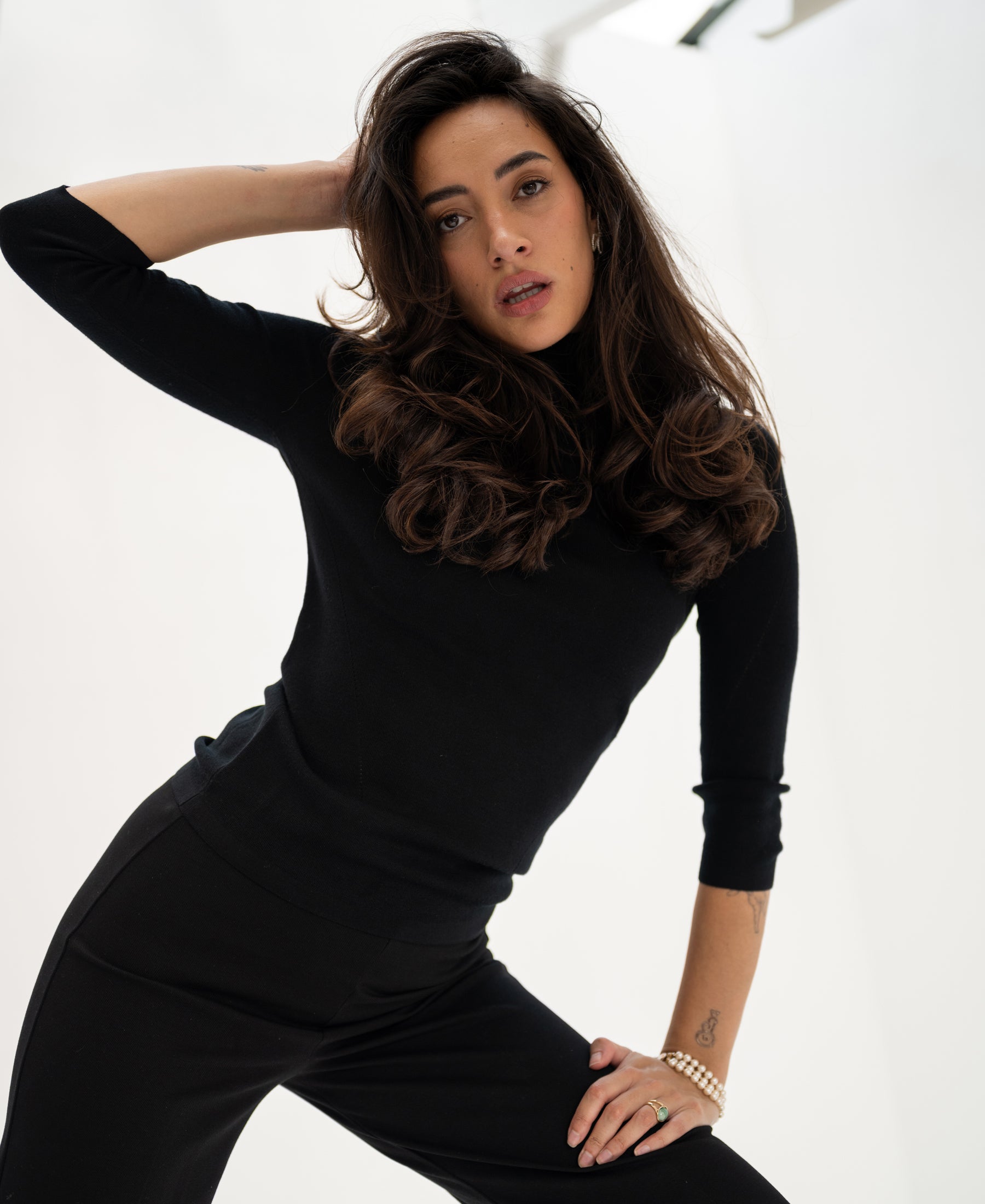Woman wearing black LE FABIAN turtleneck sweater, hand on her head.