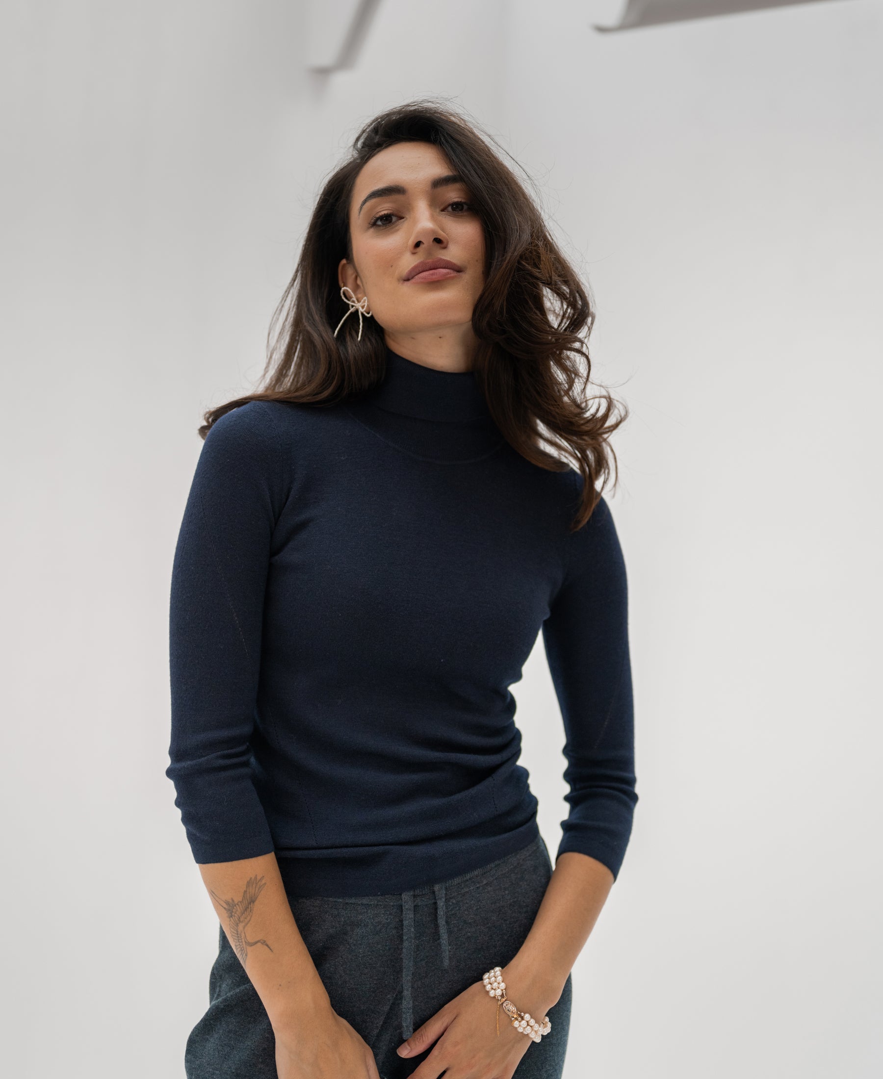 Woman wearing a PLEIN PUBLIQUE LE FABIAN dark blue turtleneck sweater, standing against a white background.