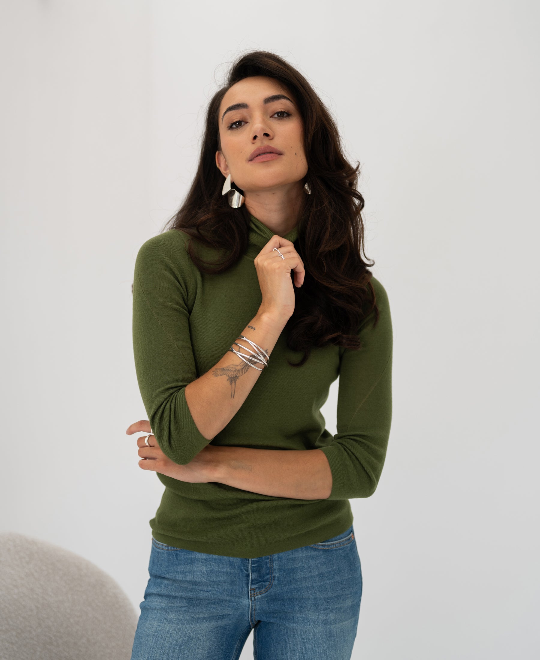 Woman wearing the LE FABIAN Olive turtleneck sweater by PLEIN PUBLIQUE against a white background.
