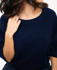 Woman wearing a dark blue PLEIN PUBLIQUE LA FRAMBOISE sweater, touching the collar with her left hand.