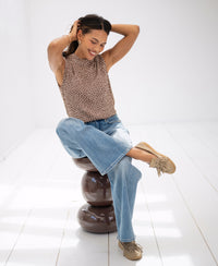 Woman wears the LA GIVERNY striped top by PLEIN PUBLIQUE, sitting cross-legged on a chair in a sunny room.