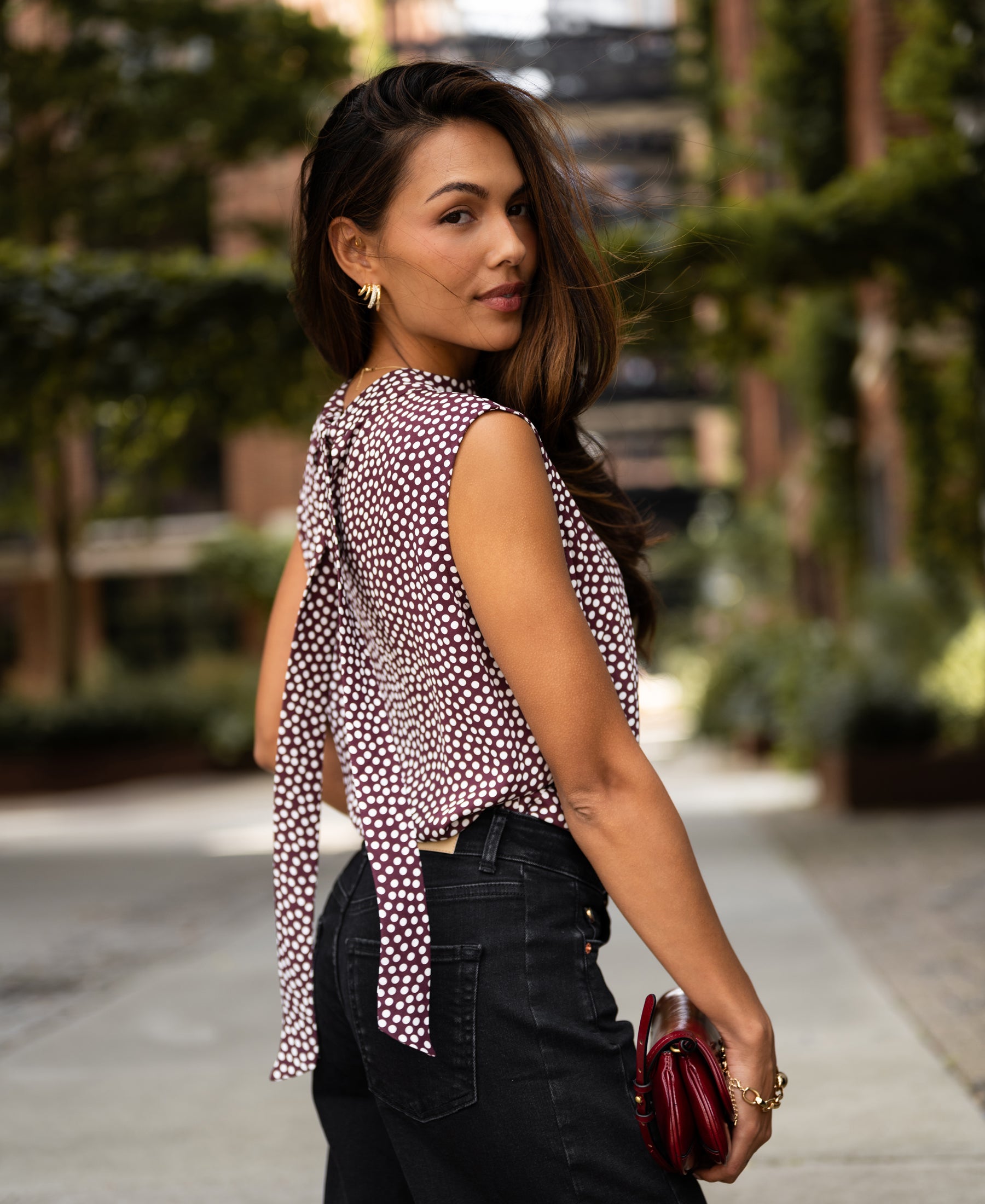 Woman wearing an ivory and wine polka dot blouse outdoors.