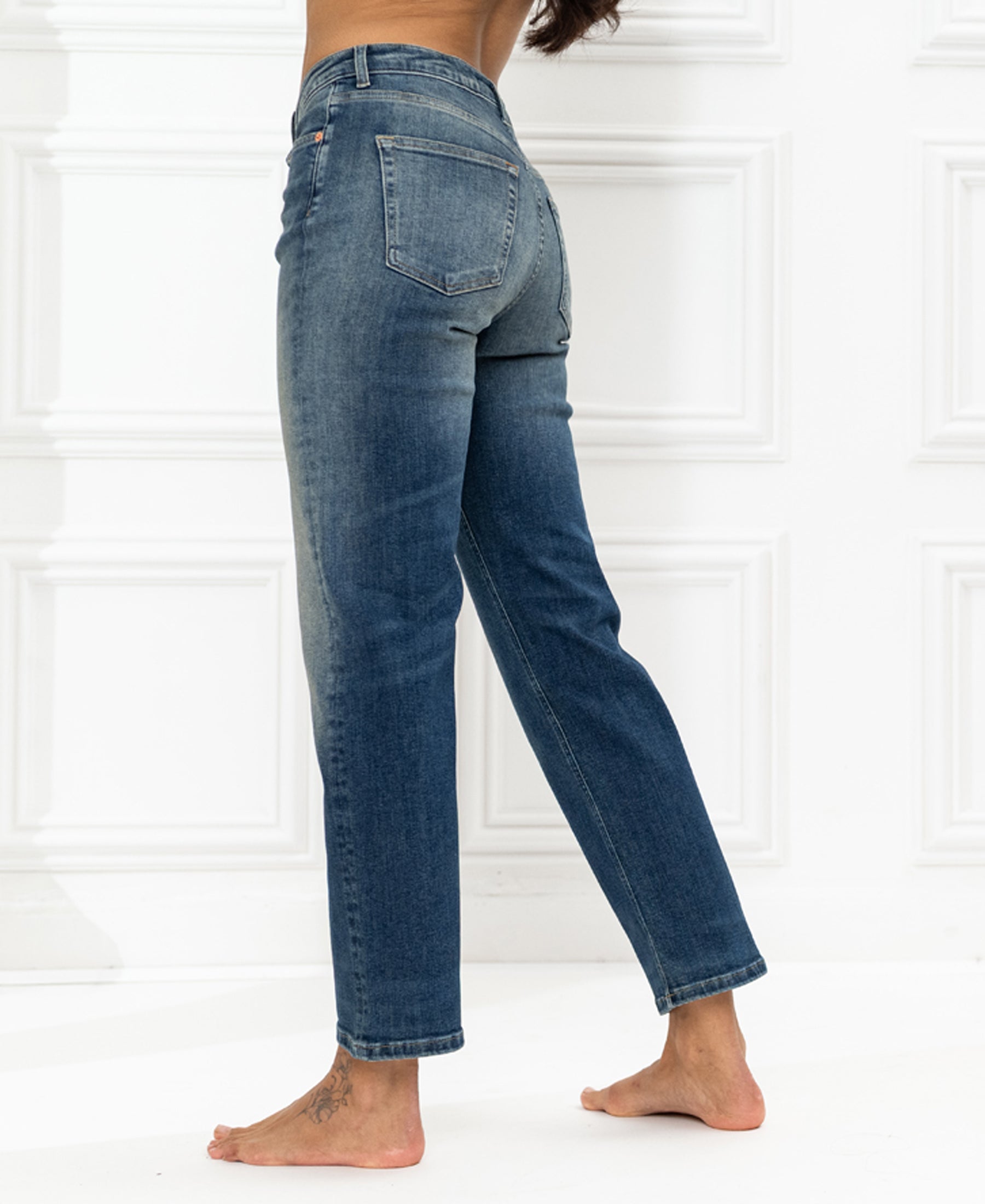 Blue vintage cropped jeans, seen from behind, modeled by a person standing on one leg by a white paneled wall.