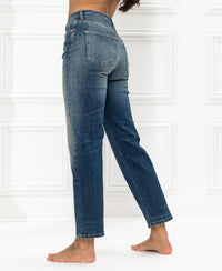 Blue vintage cropped jeans, seen from behind, modeled by a person standing on one leg by a white paneled wall.