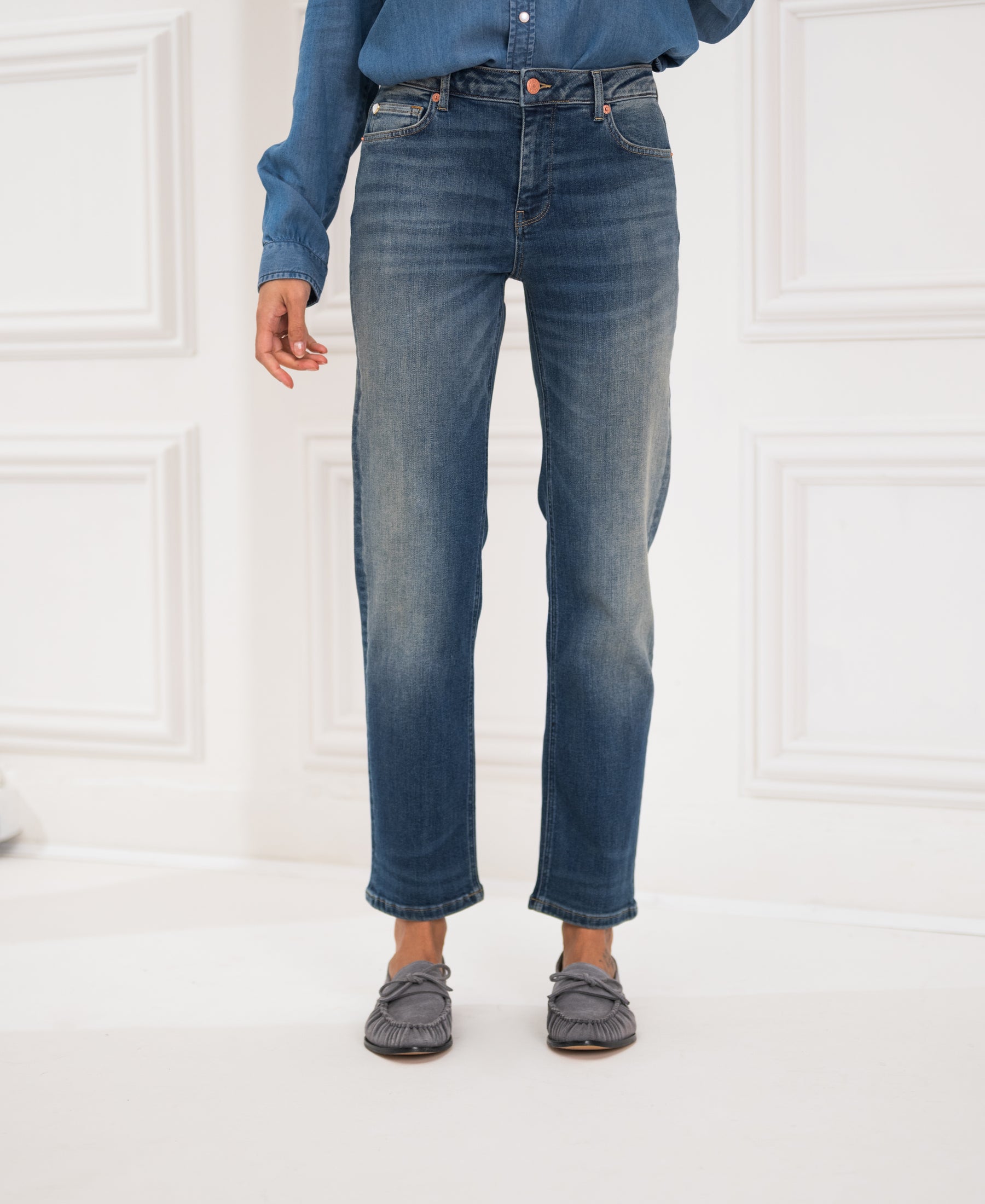 Person wearing blue vintage cropped jeans by a white wall.