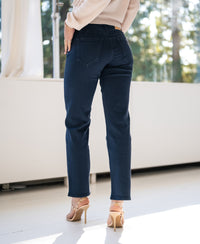 Person standing indoors facing away, wearing dark blue cropped jeans.