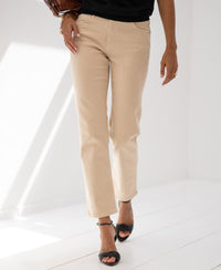 Person wearing cropped sand-colored jeans by PLEIN PUBLIQUE stands in a bright, minimalist room.