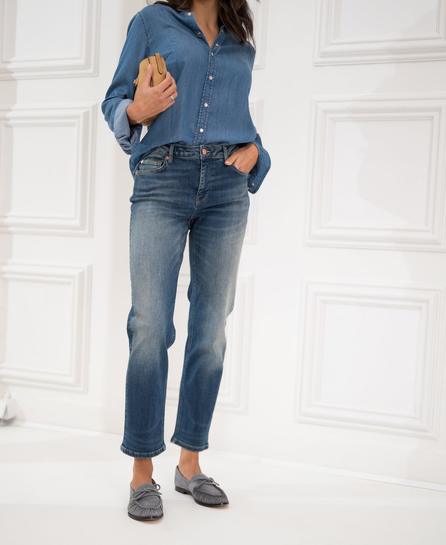 Blue vintage cropped jeans with a relaxed fit, shown on a model standing by a white paneled wall.