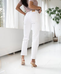 Back view of woman wearing cropped jeans in light color, standing indoors with natural light streaming through large windows.