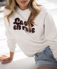 Woman wearing an ivory and cacao-colored Plein Publique La Harper sweater, shown seated in sunlight.