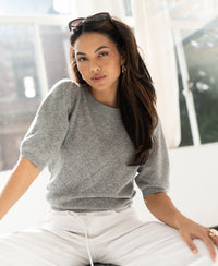 Grey argyle merino wool sweater shown on a woman sitting by a window, facing the camera.