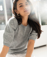 Gray argyle merino wool sweater by PLEIN PUBLIQUE, shown on a woman in a bright room.