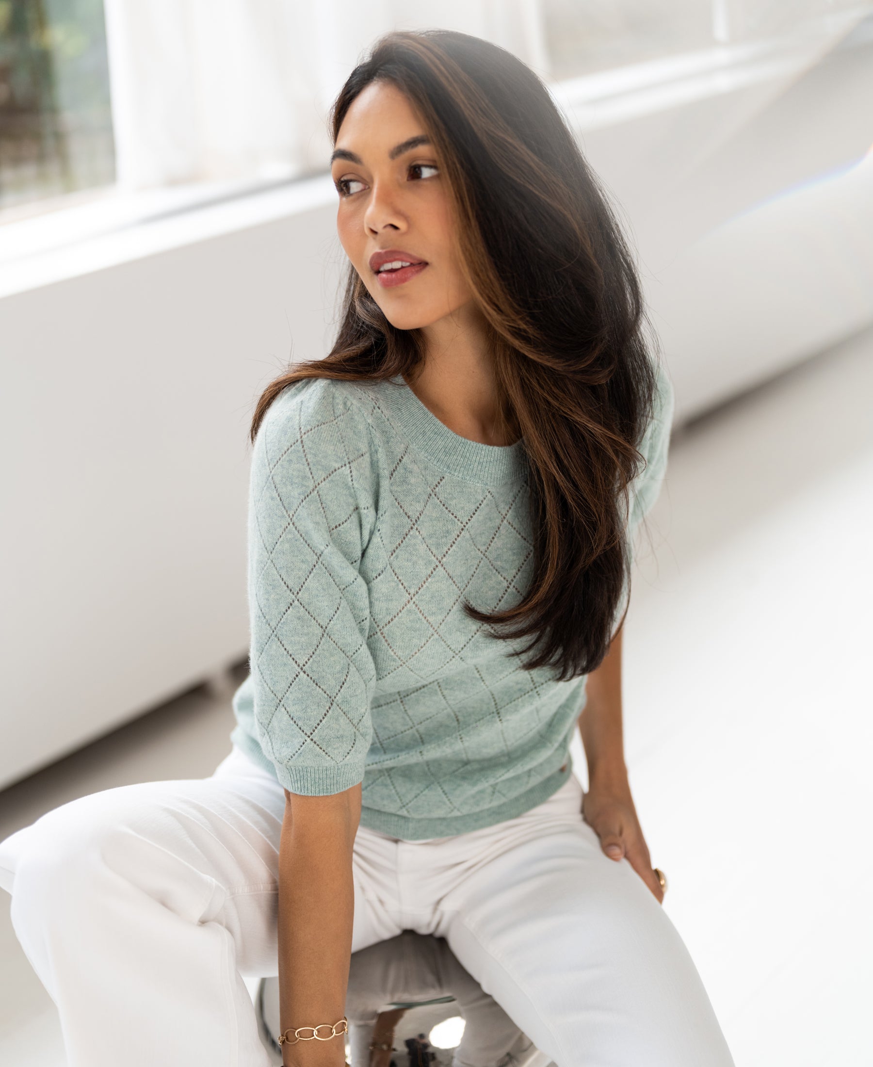 Mist green argyle merino wool sweater, shown from the front, model looking to her left indoors.