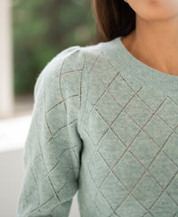 Close-up of an argyle merino wool sweater in mist green, partial view.