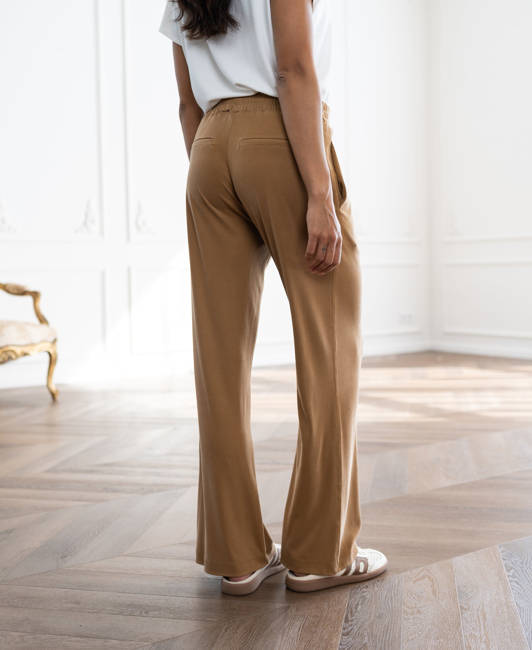 Light camel lounge pants shown indoors on a wooden floor.