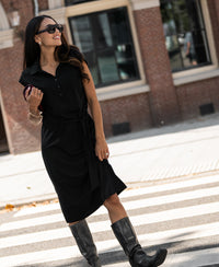 Woman wearing the PLEIN PUBLIQUE Travel polo dress INES in black, standing on a sunny city street.