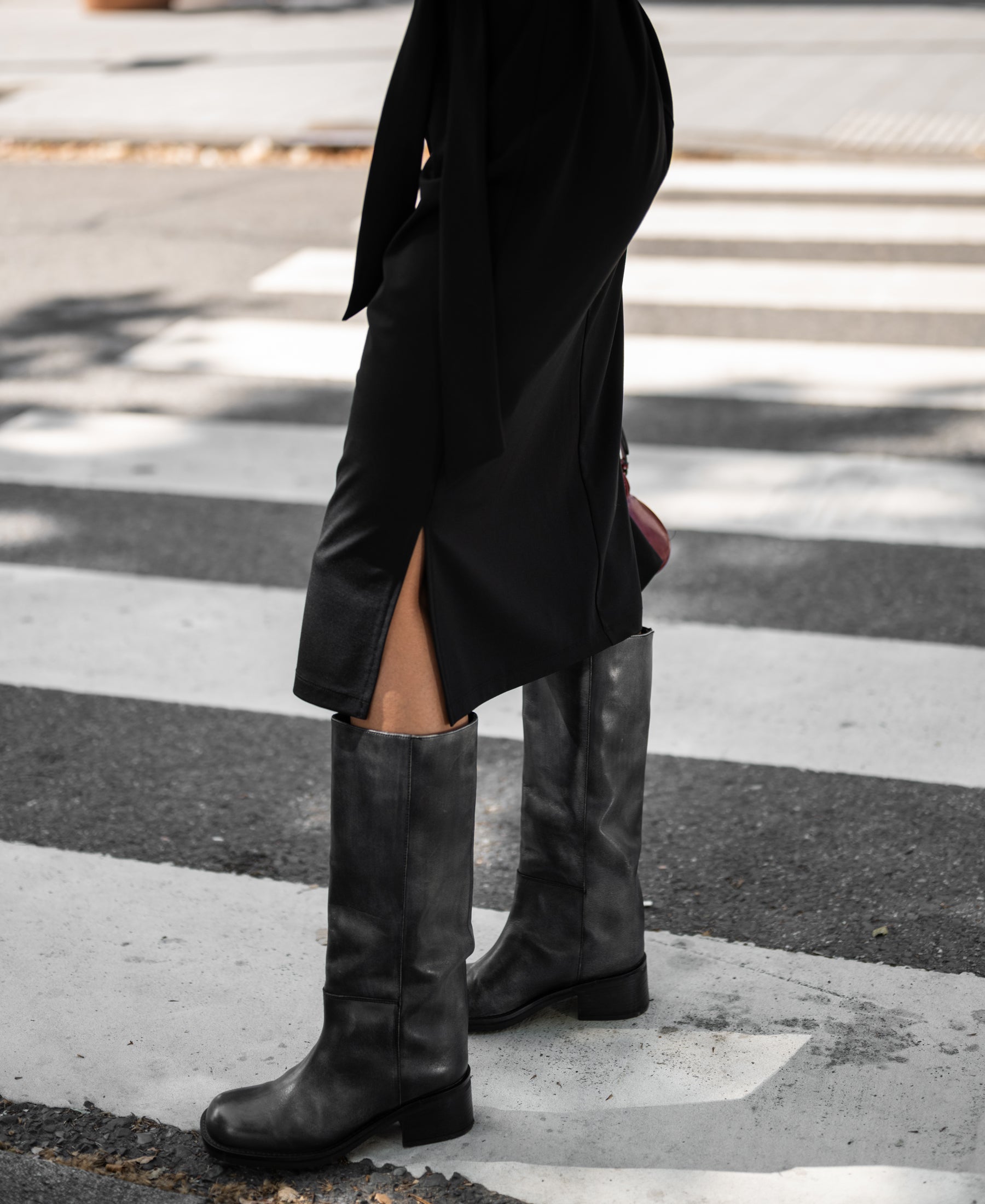 Person wearing black PLEIN PUBLIQUE Travel polo dress INES, standing on a crosswalk.