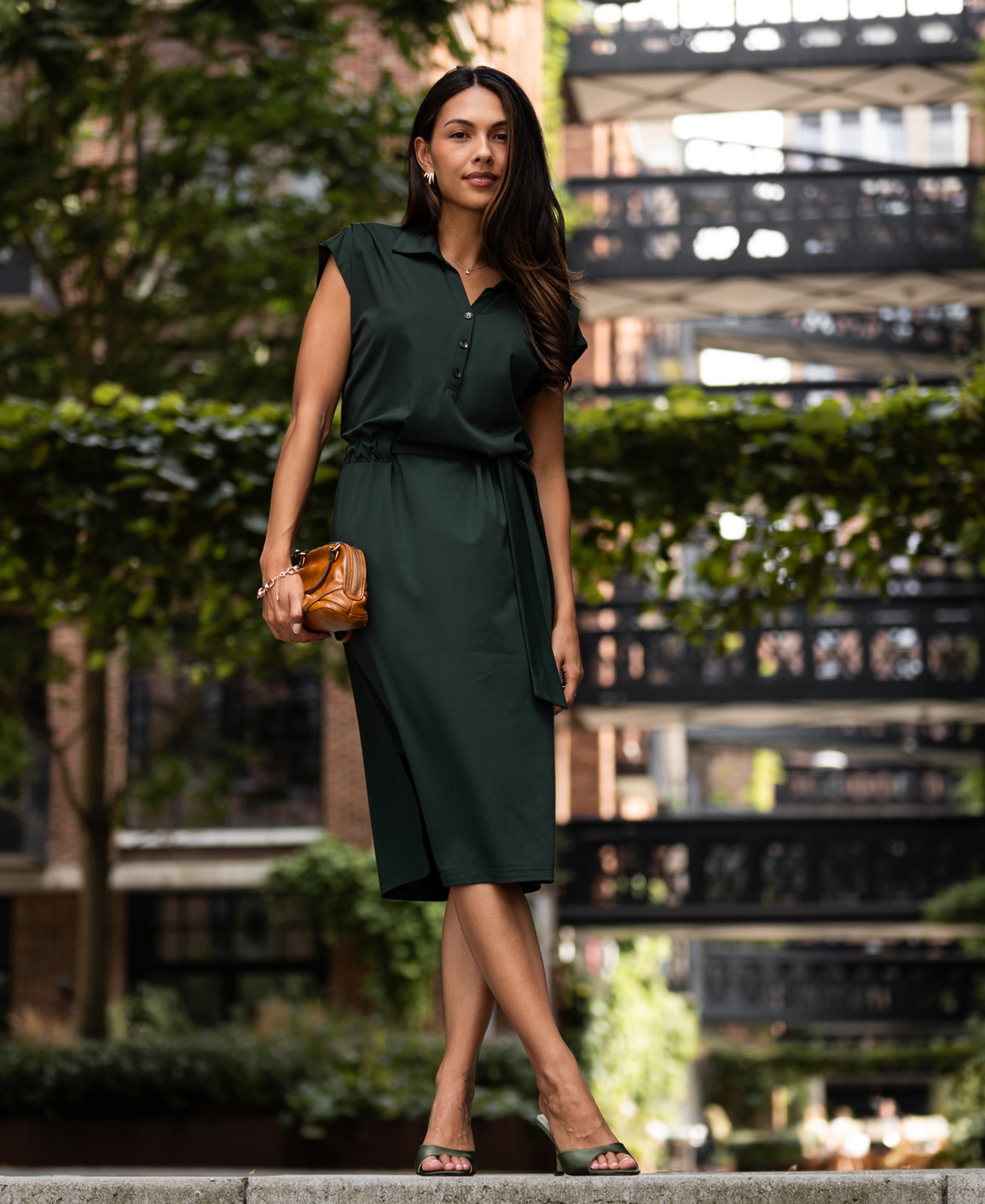 Woman wearing a dark green travel polo dress near trees.