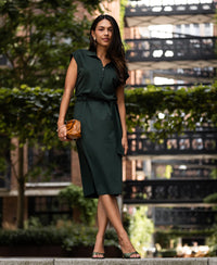 Woman wearing a dark green travel polo dress near trees.