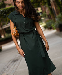 Woman wearing a dark green PLEIN PUBLIQUE Travel polo dress, standing on a city sidewalk.
