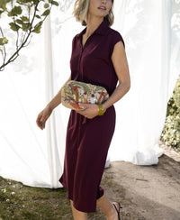 Woman wearing a wine-colored travel polo dress by PLEIN PUBLIQUE walking outdoors by white curtains.