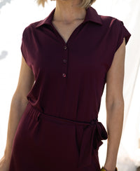 Wine-colored Plein Publique travel polo dress with buttoned front and tied waist, shown in bright light.