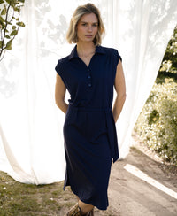 Navy blue Travel polo dress with a collar shown outdoors, with white curtains and greenery in the background.