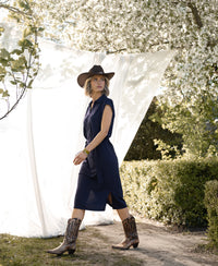 Woman wearing a navy blue PLEIN PUBLIQUE Travel polo dress INES walks outdoors near blooming trees.