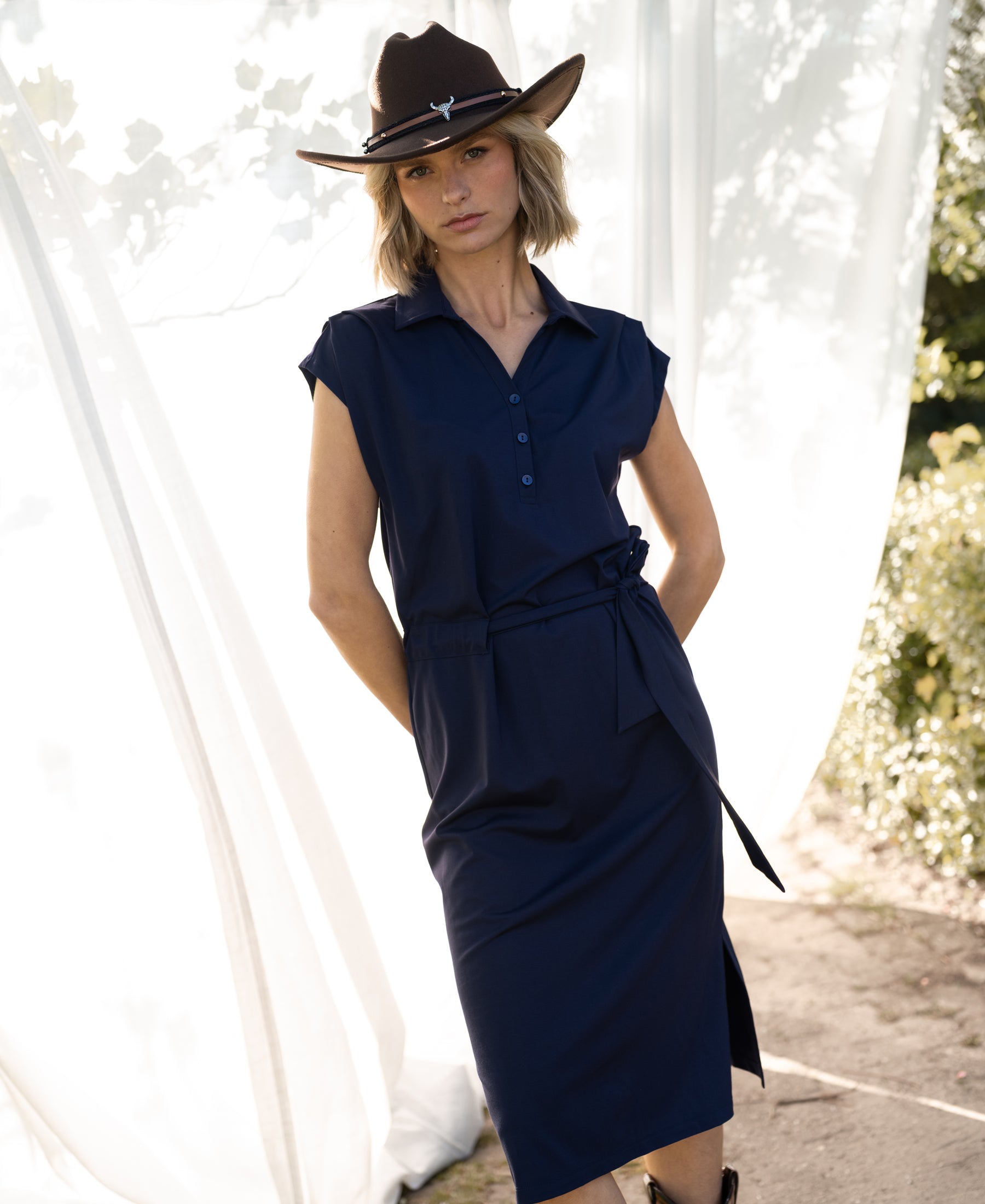 PLEIN PUBLIQUE INES navy blue Travel polo dress, shown outdoors, hands in pockets, front view.