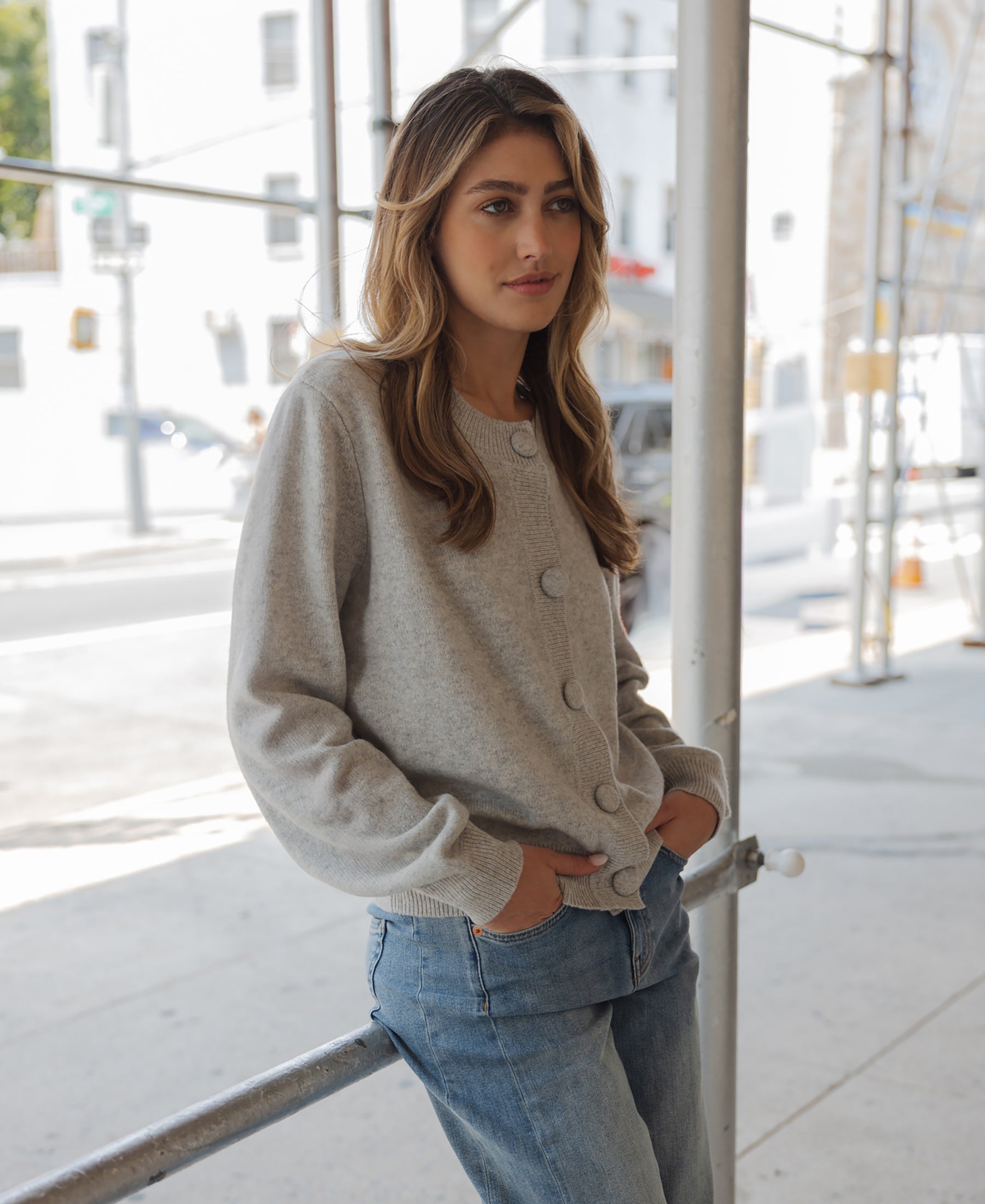 Woman wearing a light grey merino wool vest stands outdoors, leaning on a rail.