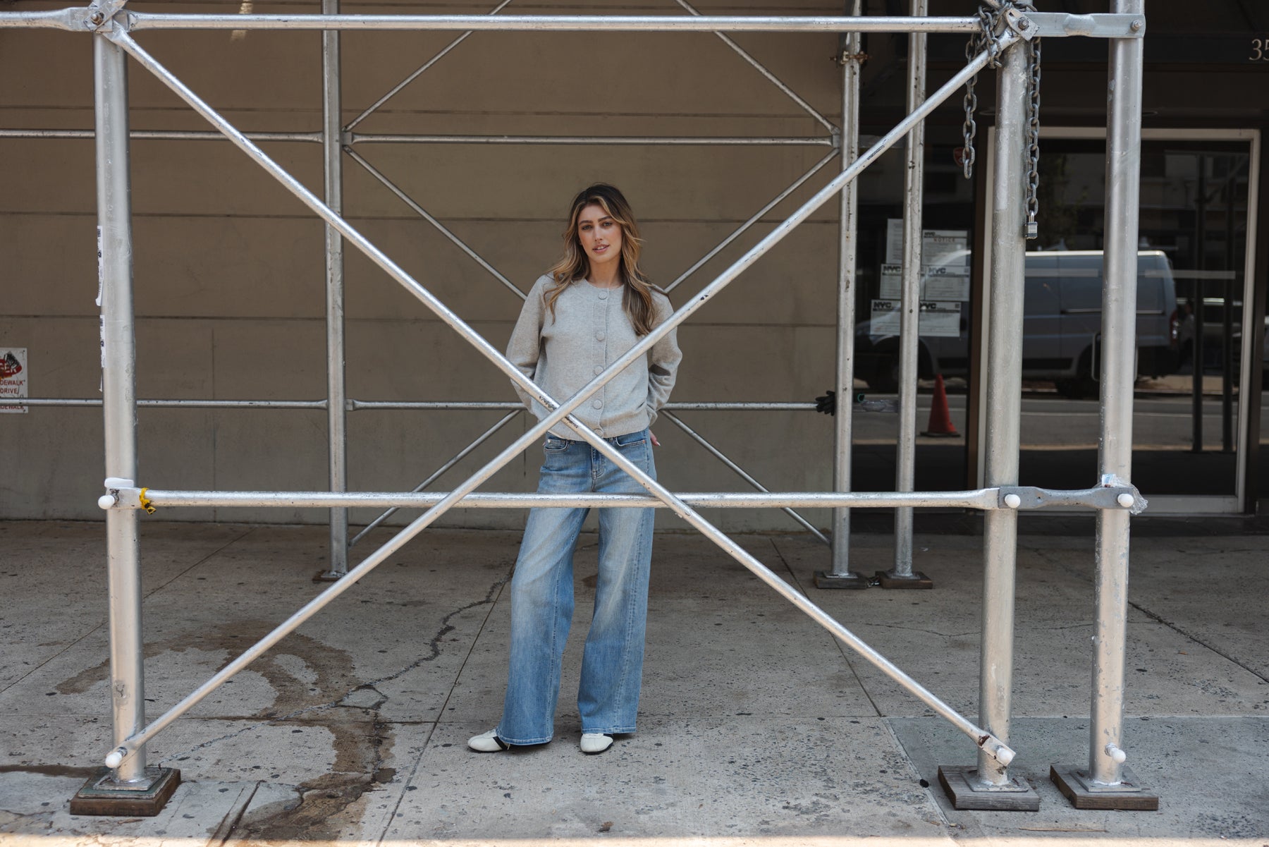 Woman wearing a light grey Merino wool vest by PLEIN PUBLIQUE stands under city scaffolding.