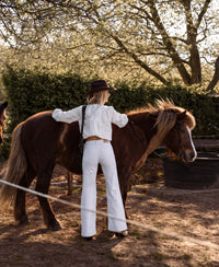 Wide leg jeans in white from PLEIN PUBLIQUE, shown on a person standing by a brown horse.