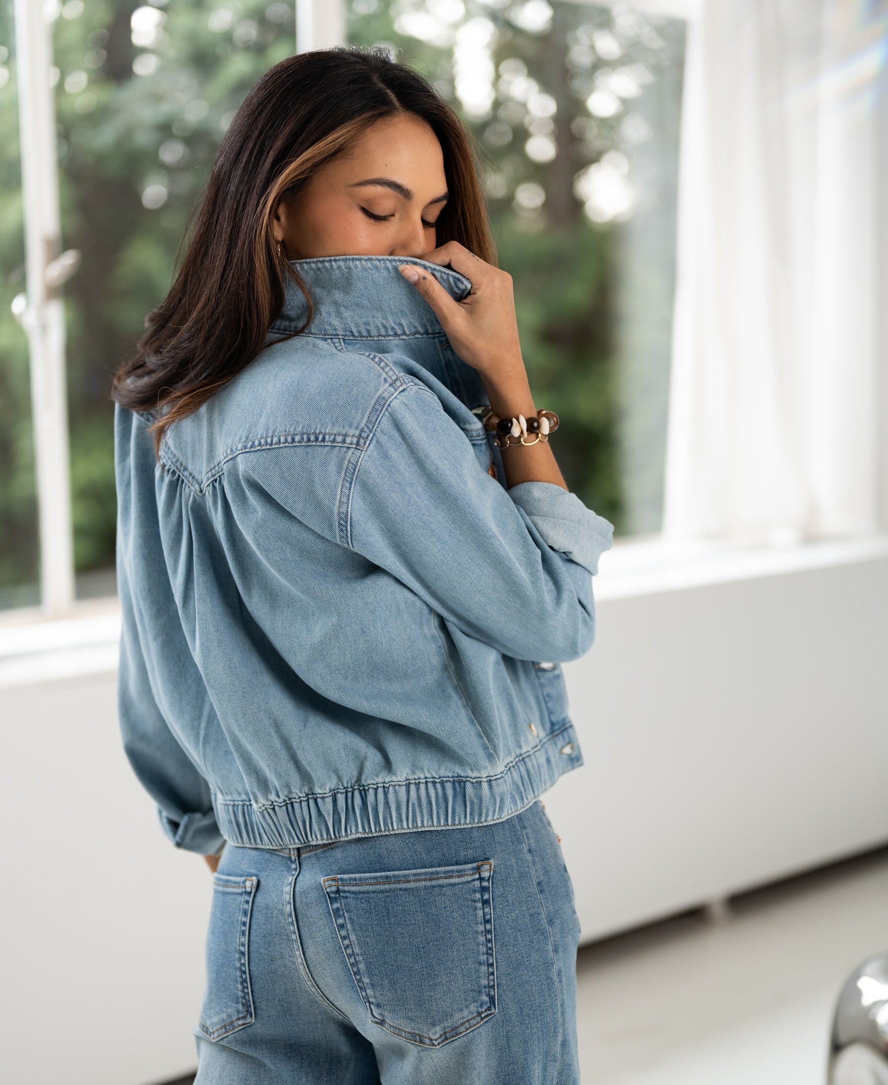 Woman indoors wearing bleached denim jacket with collar up, partially covering her face.