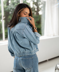 Woman indoors wearing bleached denim jacket with collar up, partially covering her face.