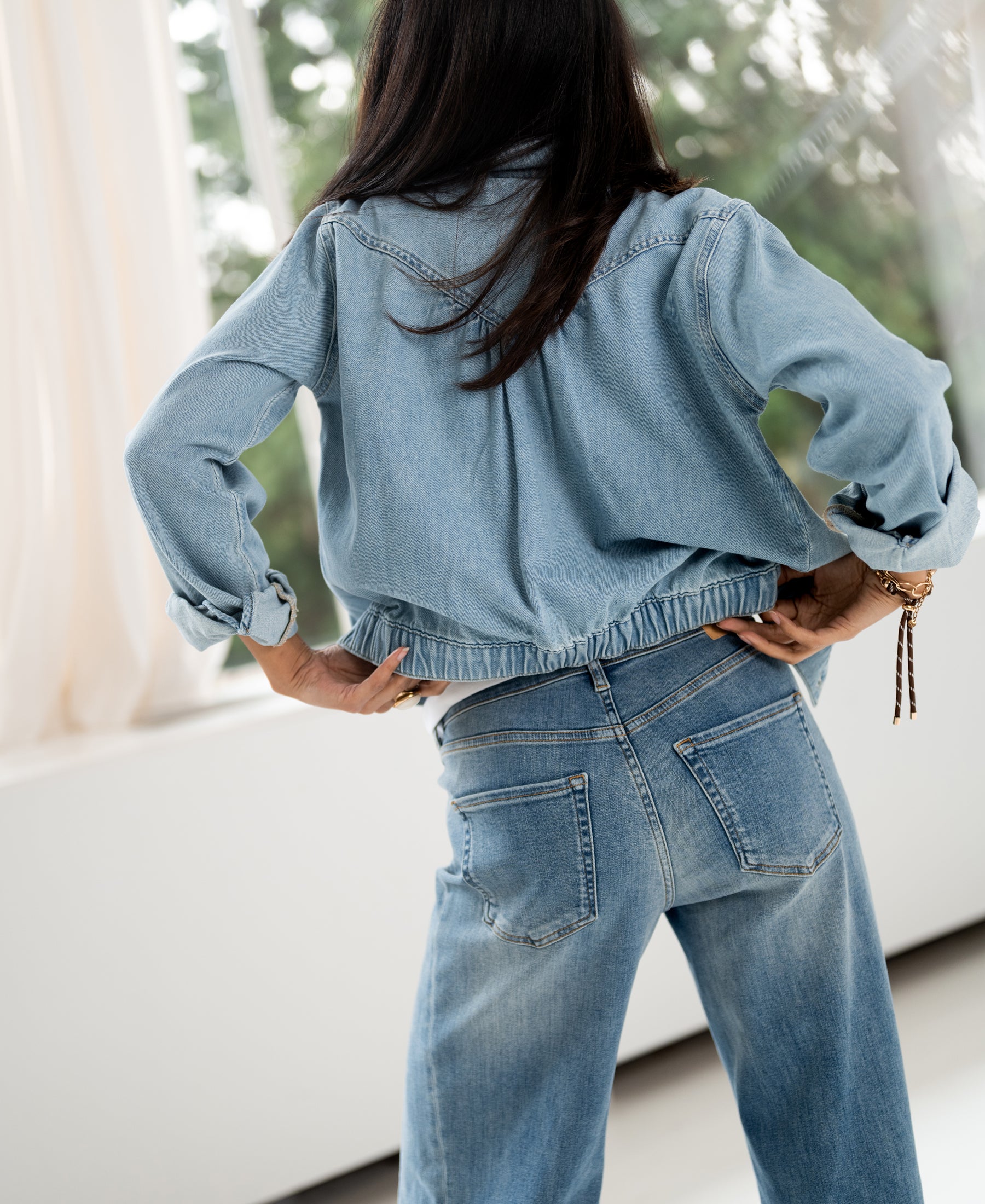 Back view of a woman wearing a bleached denim jacket, hands on hips.