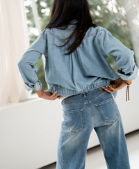Back view of a woman wearing a bleached denim jacket, hands on hips.