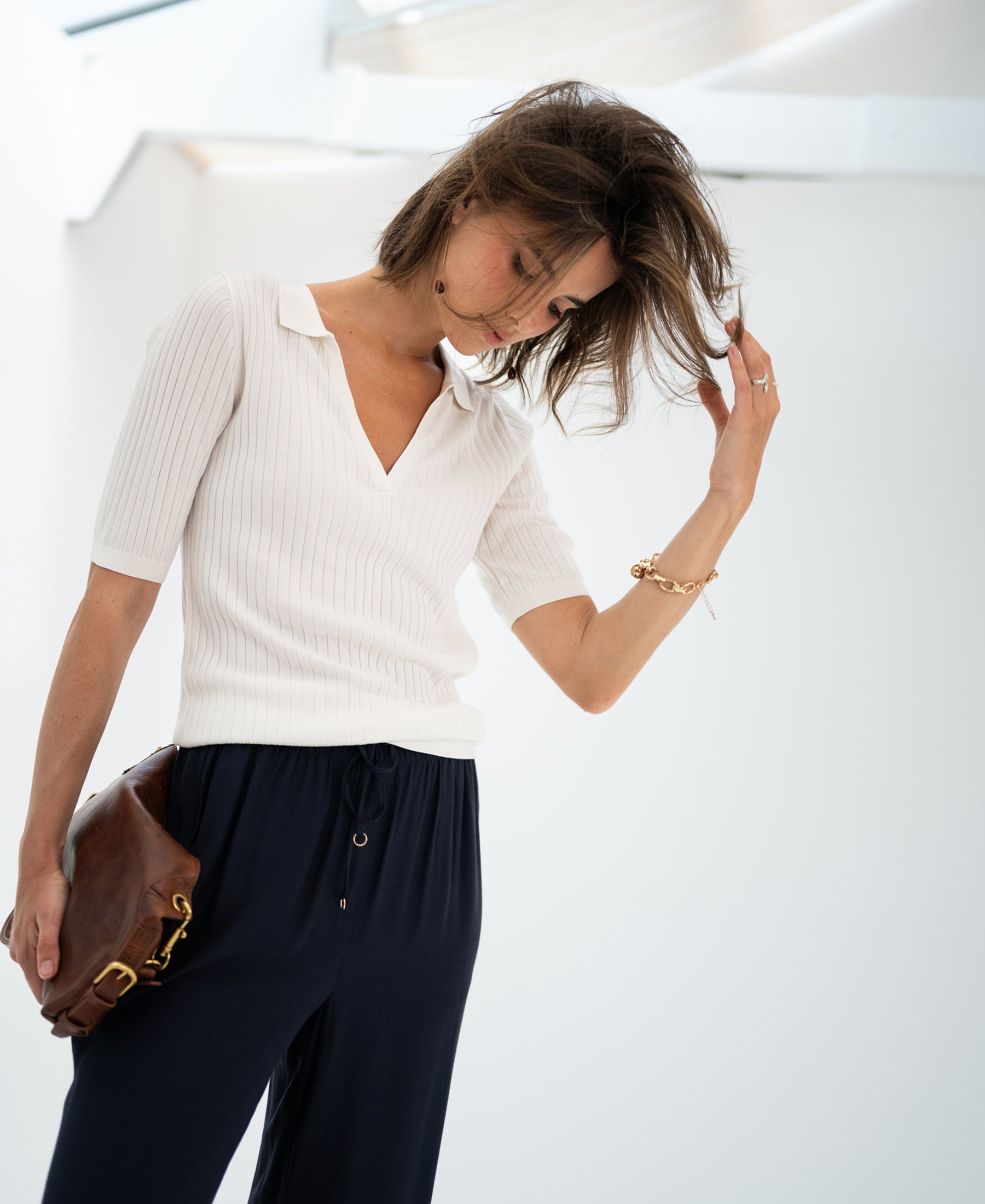 Woman in white Tencel-silk polo shirt looks down and touches her hair.