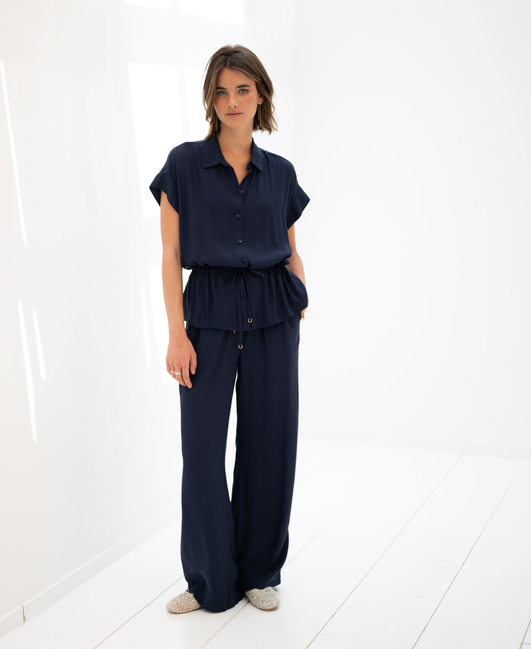 Navy blue LA JODY blouse by PLEIN PUBLIQUE shown on a woman in a minimalist white room.