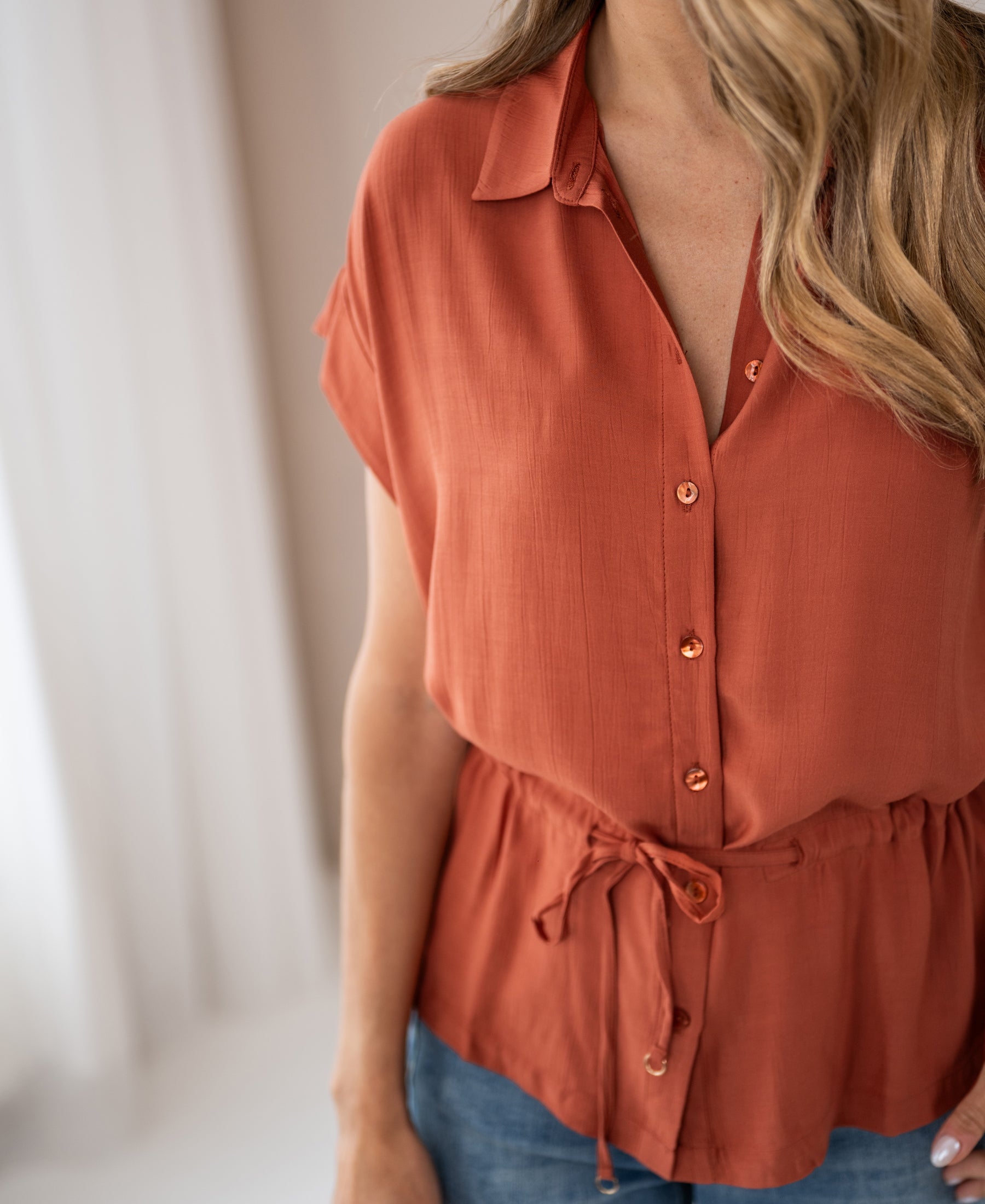 Terra-colored LA JODY blouse with waist tie by PLEIN PUBLIQUE, shown indoors.